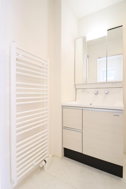【1号棟】洗面化粧台　洗面化粧台の横にあるパネルヒーターは、タオル掛けとしてお使いいただます。