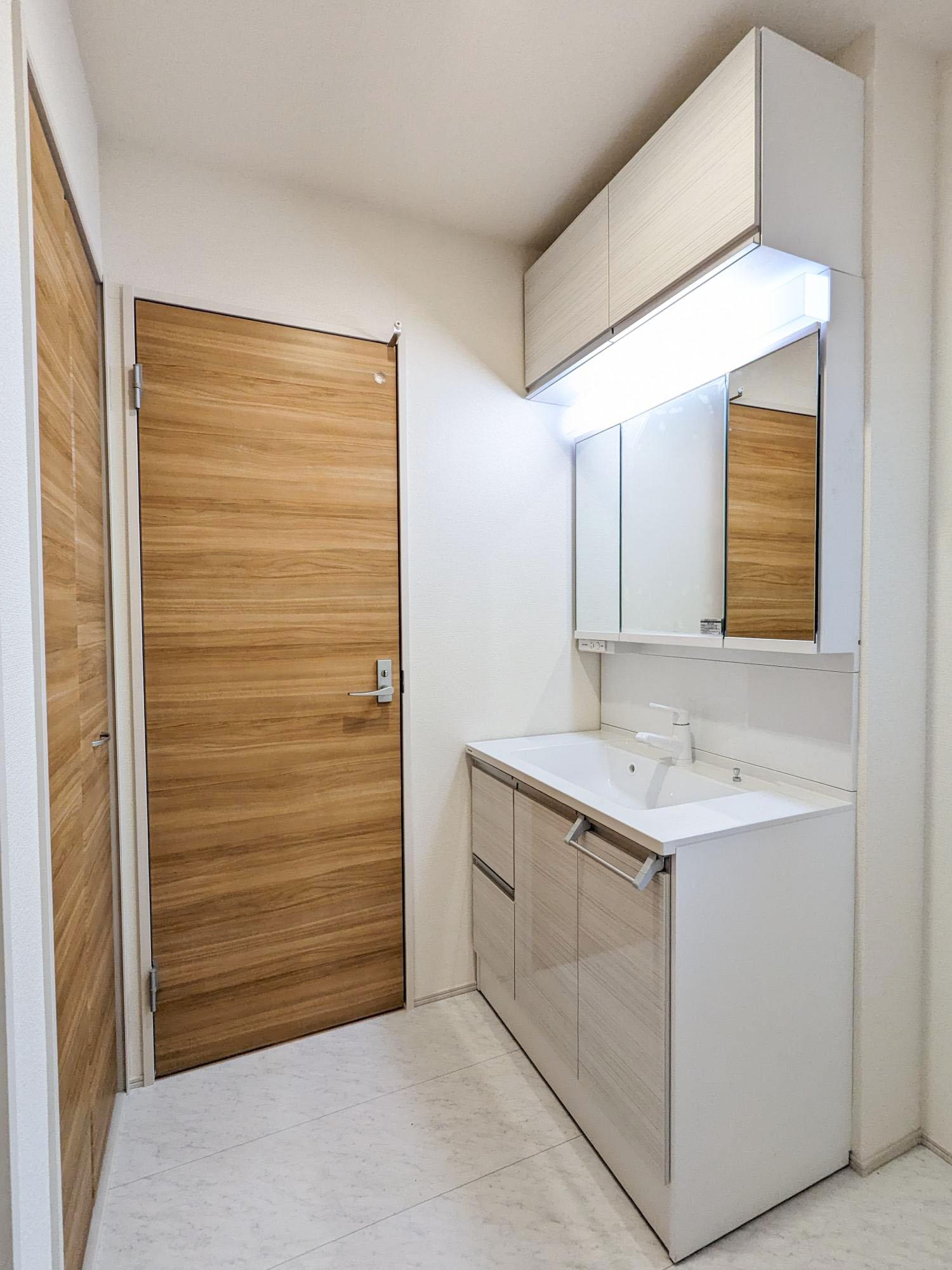 【1号棟】　ナチュラルカラーでまとめられた洗面所は、横幅が900mmワイドの三面鏡付きで朝の身支度もラクラク。吊り戸もあり収納スペースにも困りません。