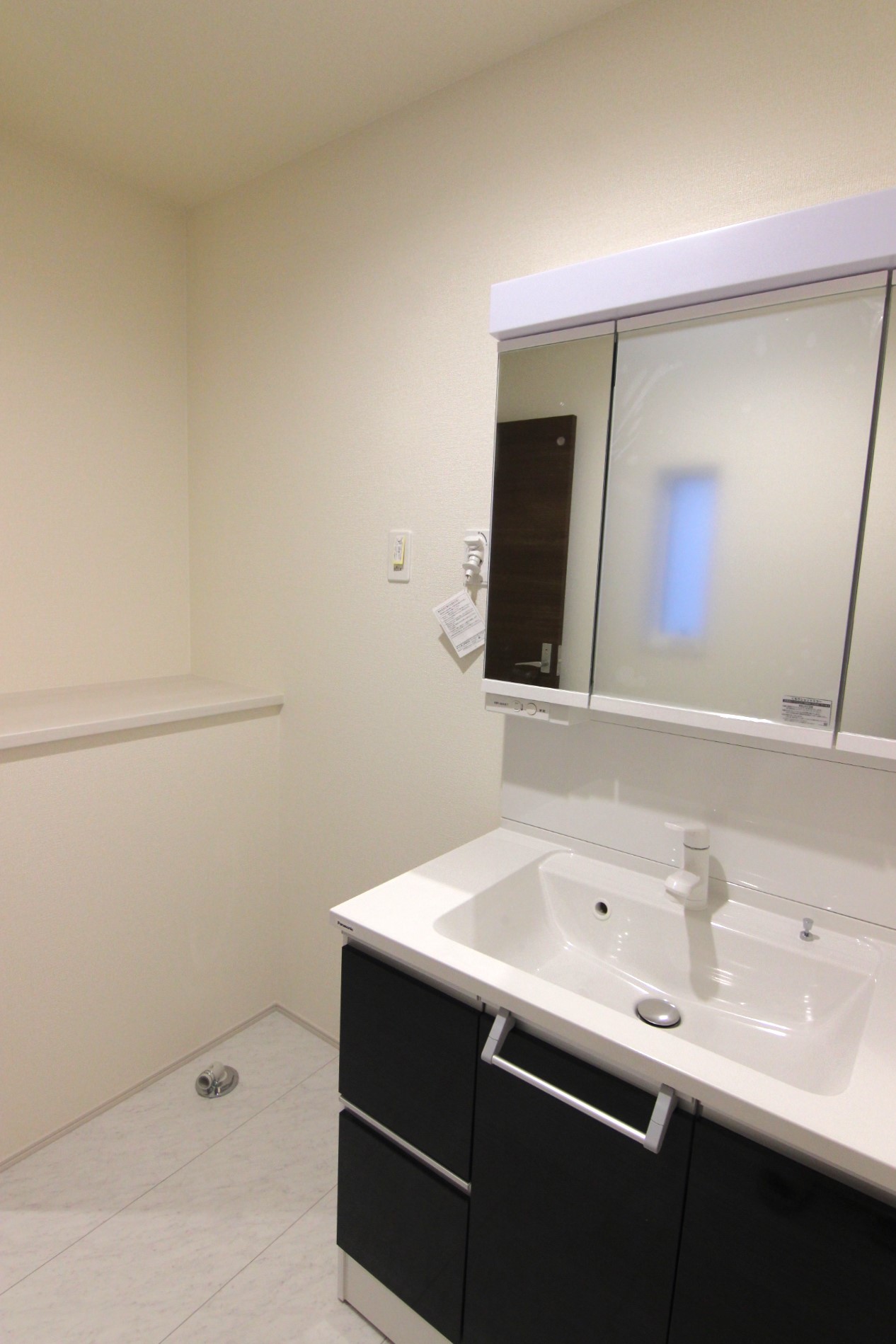 【1号棟:洗面所】　白を基調とした空間にシックなダークブラウンが映える清潔感ある洗面所。洗面台は、三面鏡の裏がコンセント付きの収納スペース!カウンタースペース・床下収納付き。