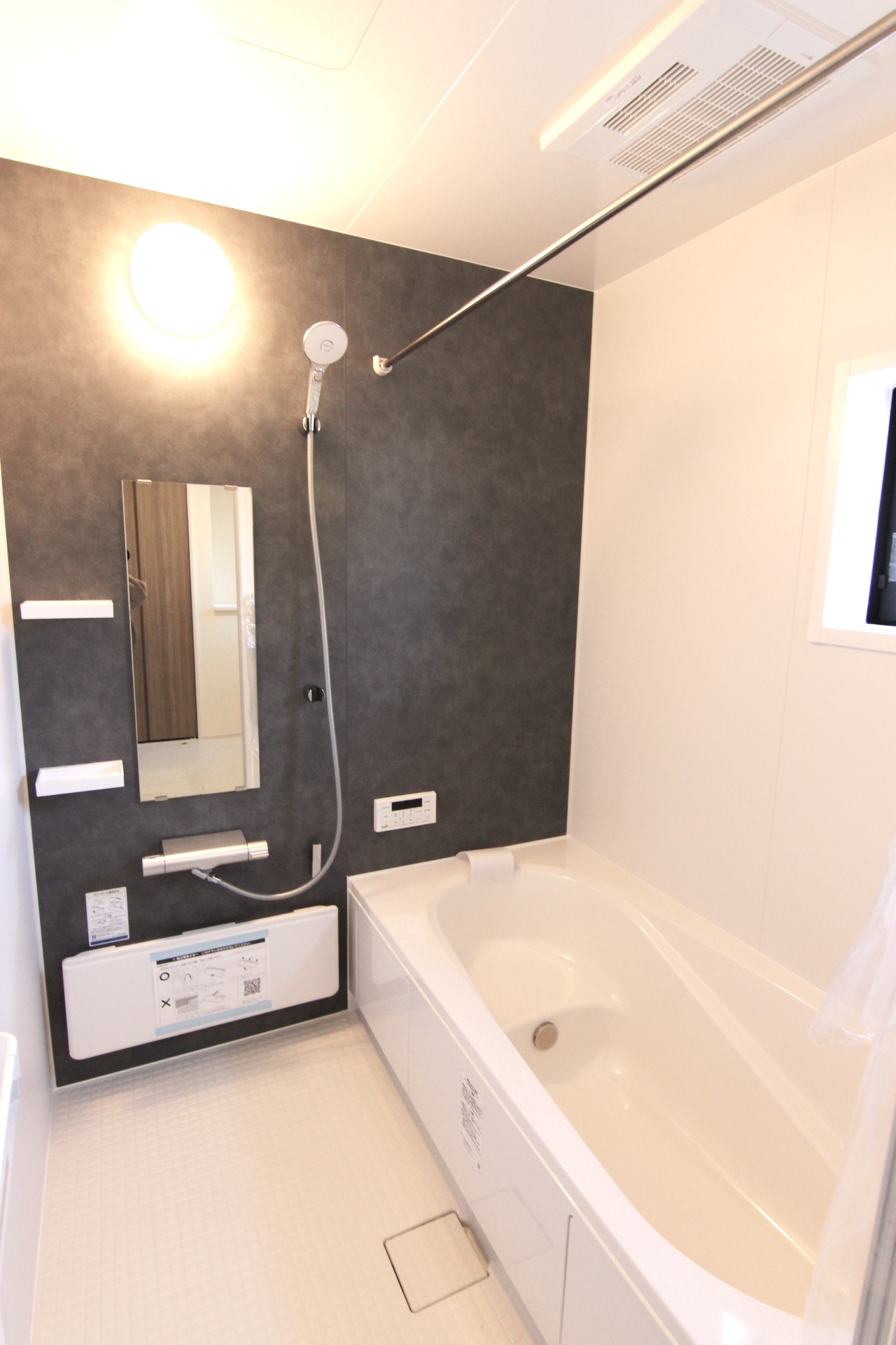 【1号棟浴室】　白を基調とし、モルティオダークの壁を一面に敷いたシックな浴室。浴室暖房換気乾燥機付で冬は温かく、雨の日のお洗濯も安心。