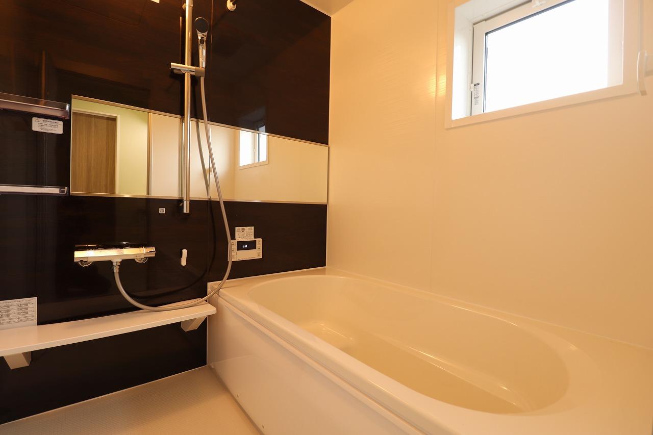 【1号棟/浴室】　ワイドミラーやシャワー用スライドバーを採用した、ホテルライクな浴室です。浴槽内はステップ付きのため、半身浴を楽しめるほか、お子様との入浴時にも重宝しそうです。