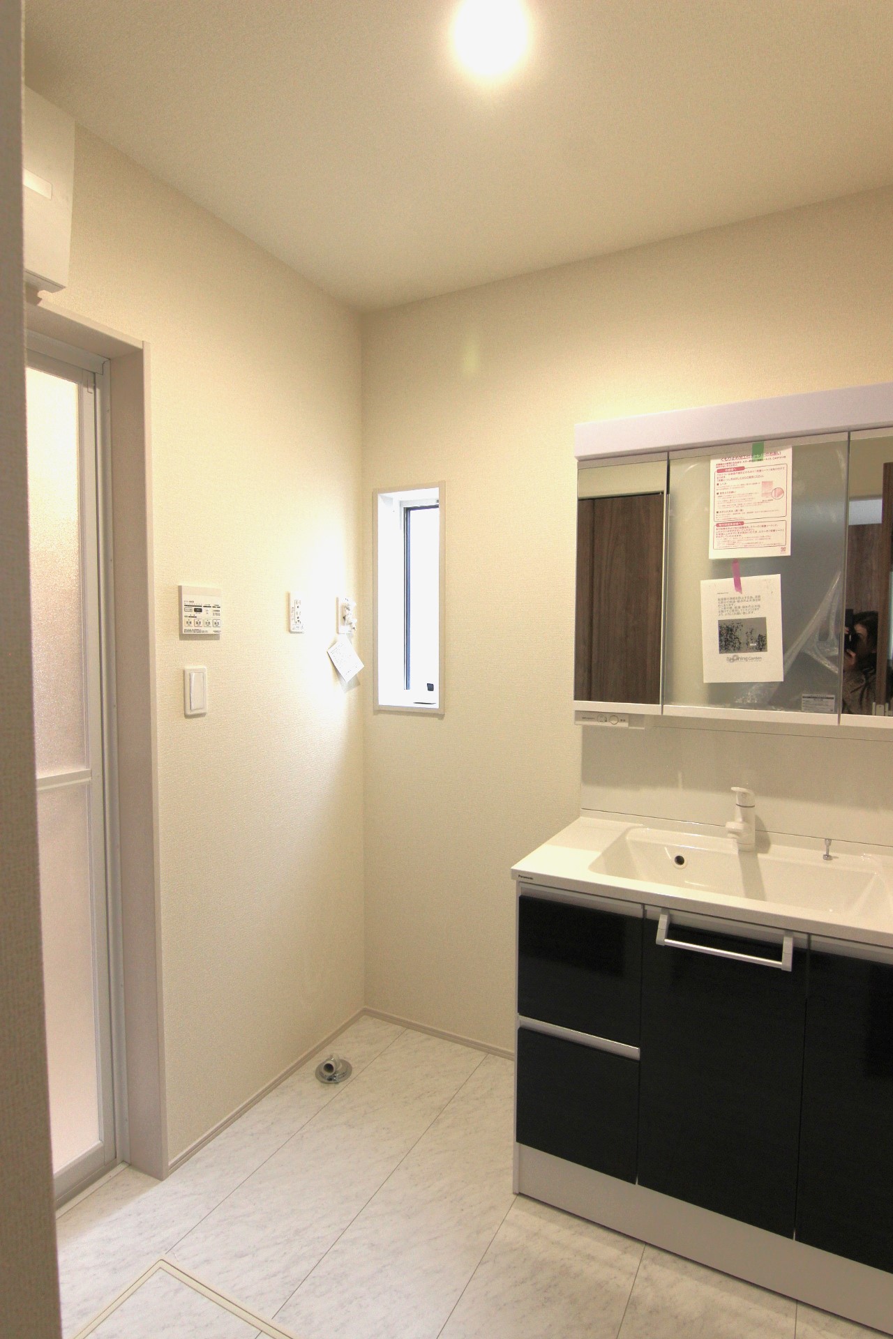 【1号棟:洗面所】　白を基調とした空間にシックなダークブラウンが映える清潔感ある洗面所。洗面台は、三面鏡の裏がコンセント付きの収納スペース!床下収納付き。
