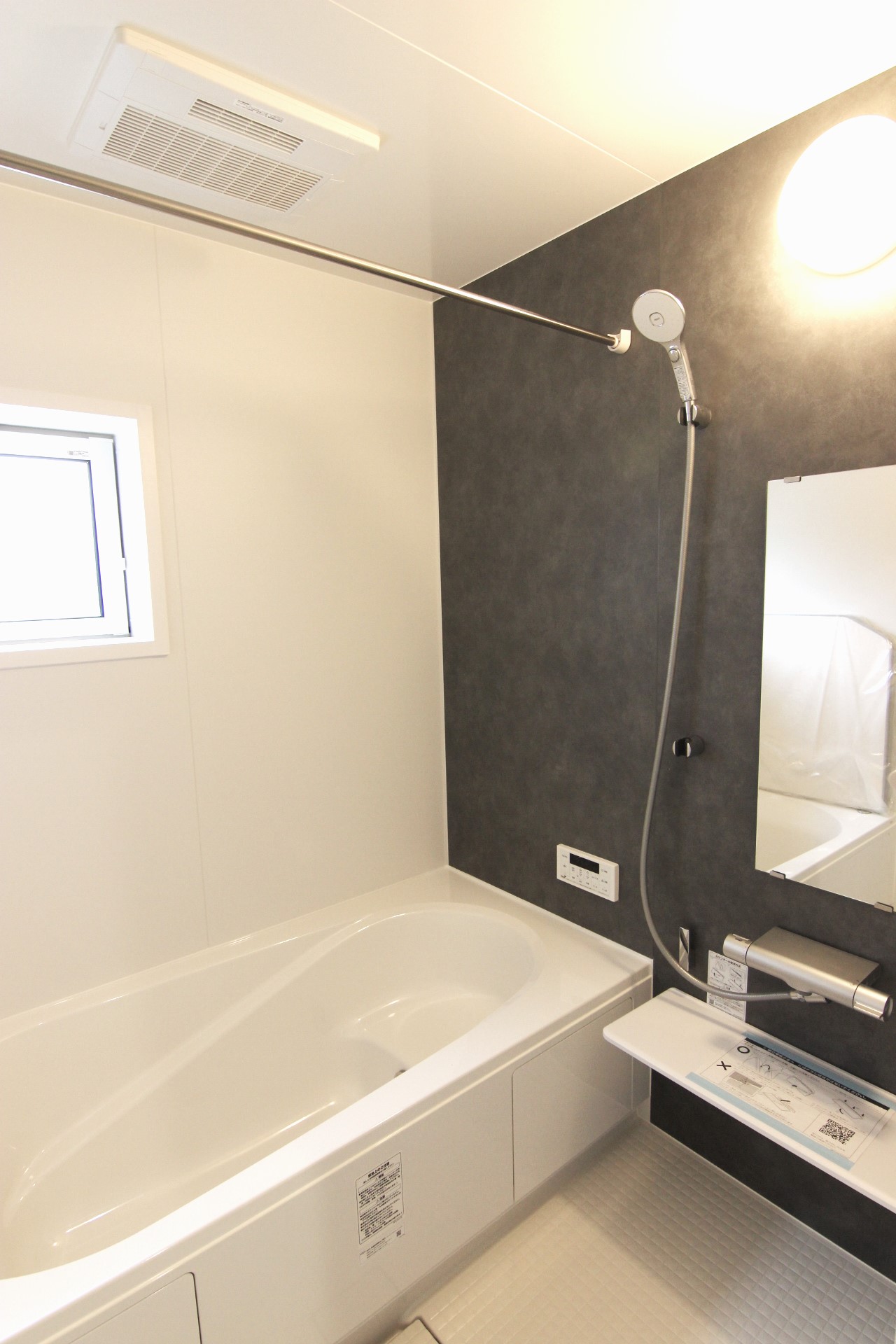 【1号棟:浴室】　白を基調とし、モルティオダークの壁を一面に敷いたシックな雰囲気の浴室。浴室暖房換気乾燥機付で冬は温かく、雨の日のお洗濯も安心。浴槽は温かさが続くサーモバスS構造。