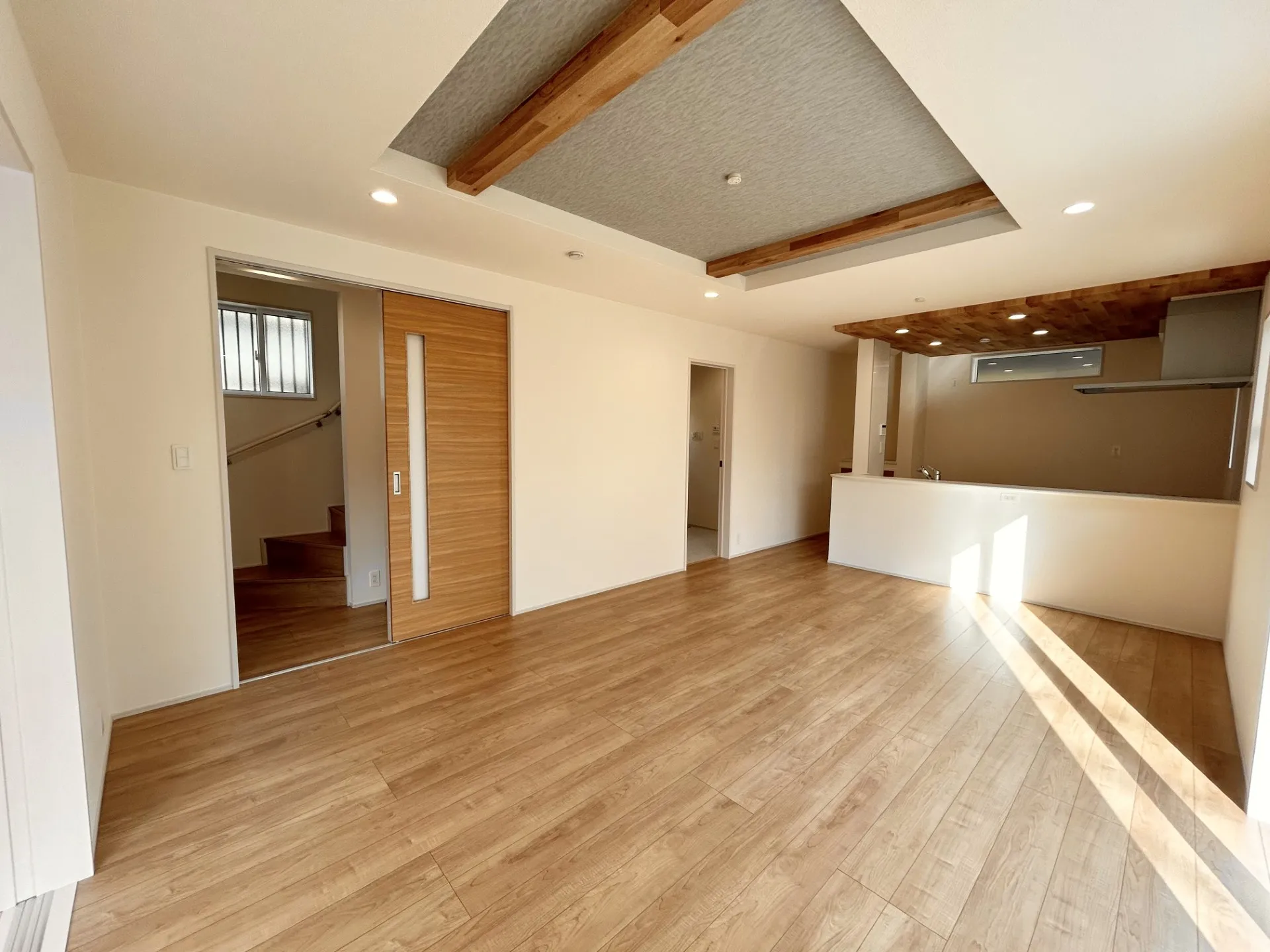 【リビング】キッチン部分と折上天井の梁部分に同一の木目調のアクセントクロスで統一感を出しました