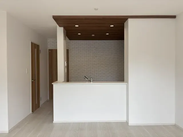 【キッチン(7号棟)】木目調の下がり天井とレンガ調のアクセントクロスが空間にアクセントを添える、おしゃれな対面キッチン。