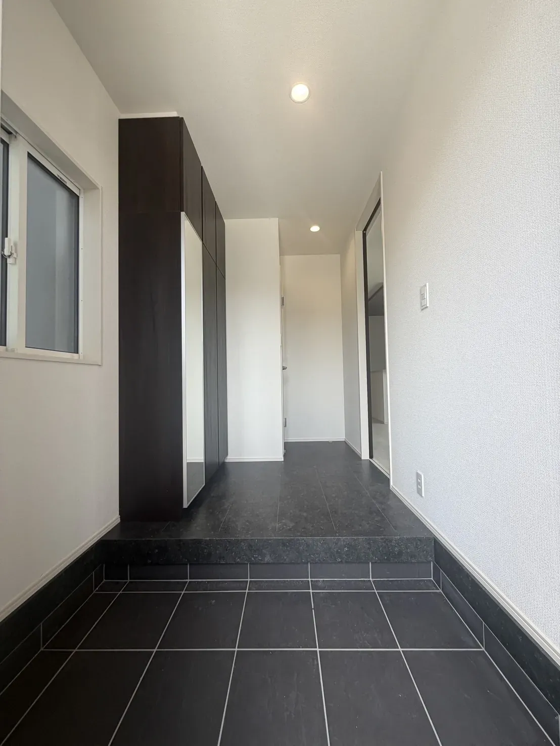 【玄関②号棟】ブラックを基調としたシックな玄関が、住まいに上質な印象を演出。タイル仕上げの落ち着いた空間に収納も備え、美しさと使いやすさを兼ね備えています。